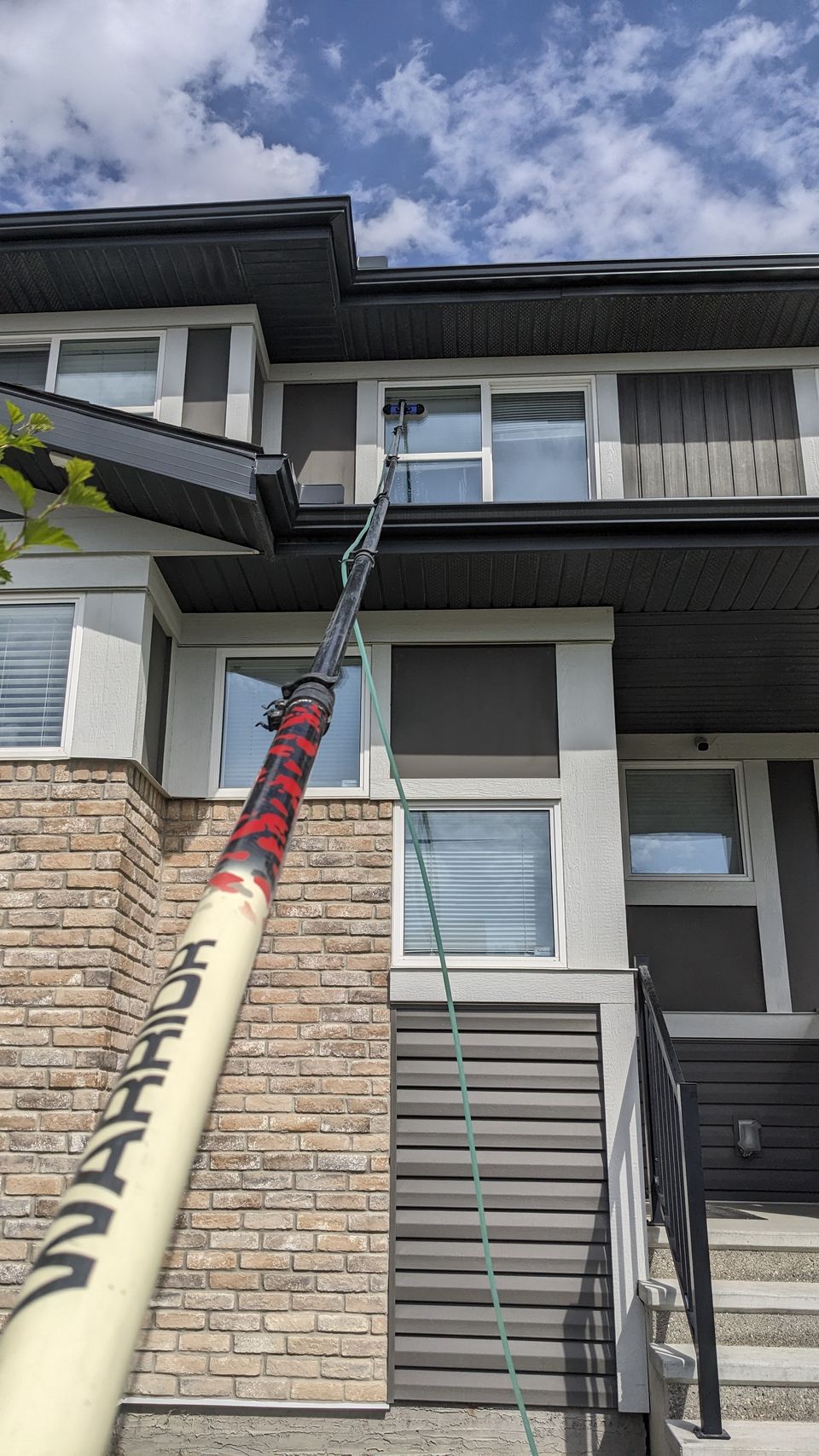 Water-fed pole cleaning a second-storey window on a Calgary townhome — Oriole Cleaning Services